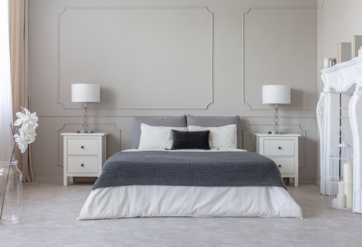 Grey blanket on white bedding on comfortable king size bed, two nightstand with lamps on both sides of it