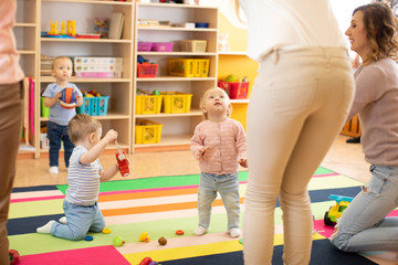 Group of babies children playing colorful educational toys together with mothers in nursery room