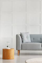 Wooden coffee table next to grey couch with pillow in white elegant interior