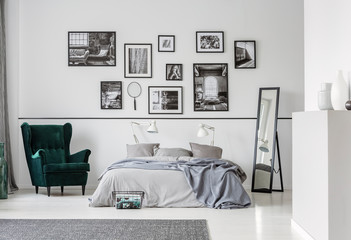 Fototapeta na wymiar Grey bed between armchair and mirror in bedroom interior with gallery and lamps. Real photo