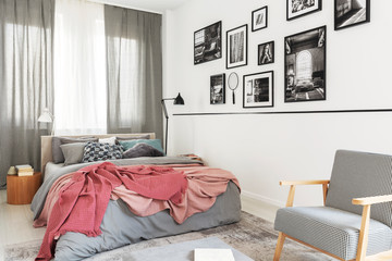 Armchair next to bed with pink blanket in modern bright bedroom interior with gallery. Real photo