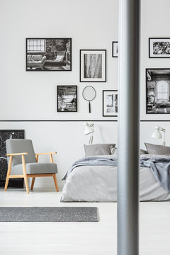 Wooden armchair next to bed in grey and white bedroom interior with gallery of photos. Real photo
