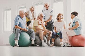 Group of happy senior sitting on exercising balls in bright fitness center before training - obrazy, fototapety, plakaty