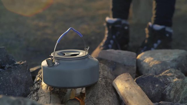 woman sitting near the campfire and boiling water in tea pot