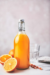 Bottle of healthy organic orange juice with oranges, glass and straws on white marble table over pink background. Summer drink. Copy space for text.