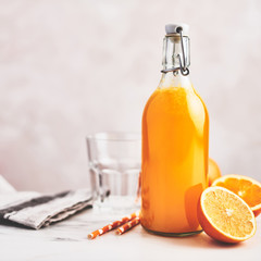 Bottle of healthy organic orange juice with oranges, glass and straws on white marble table over pink background. Summer drink. Copy space for text. Square crop.