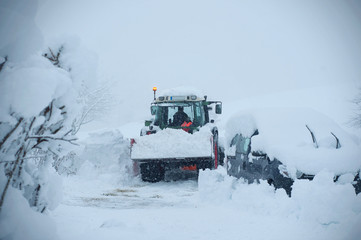 Winter service tractor cleaning the road surface. A car locked in the snow, after a snow cyclone.