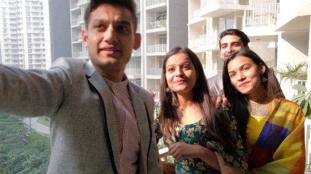 Friends taking selfies photo at a terrace balcony in sun with apartment high rise skyline elevation in the backdrop, gimbal stabilized handheld  