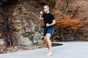 Strong concentrated young man in a t-shirt and shorts engaged in martial arts in nature. Concept of self-improvement and sports training