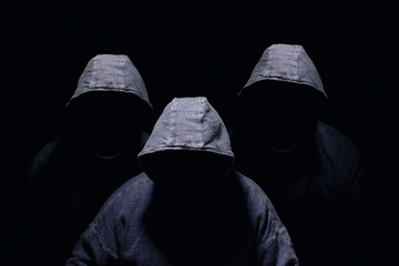 Three mysterious men silhouette with darkened face, no visible face, in blue hoodies on dark...