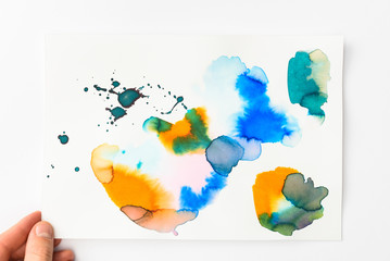 Man holding paper with abstract watercolor blue, golden and yellow spills on white background