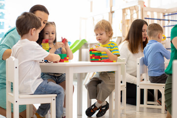 Preschool teacher with kids playing with colorful wooden educational toys at kindergarten