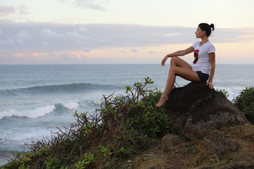 Girl posing sitting sideways on a stone cliff against the background of the sea and sky