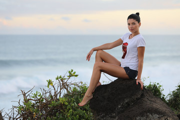 Girl posing sitting sideways on a stone cliff against the background of the sea and sky