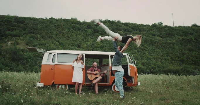 Man spinning woman around next to friends in vintage van