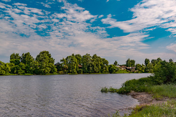 Fototapeta premium Landscape, beautiful summer. A village on the Bank of a wide river, beautiful, Cumulus clouds on a blue sky on a summer day.