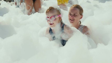 Funful children's holidays with the whole family, a young active woman with her little daughter are having fun frolicking on a foam party at the seaside