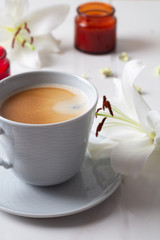 cup of coffee, white lilies and candles close up on a white background.