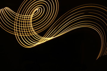 Light painting, long exposure photography, metallic gold yellow color against a black background