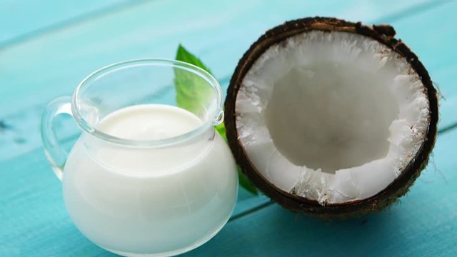 Closeup shot of composed glass of milk and coconut half with mint leaves on blue-colored wooden table