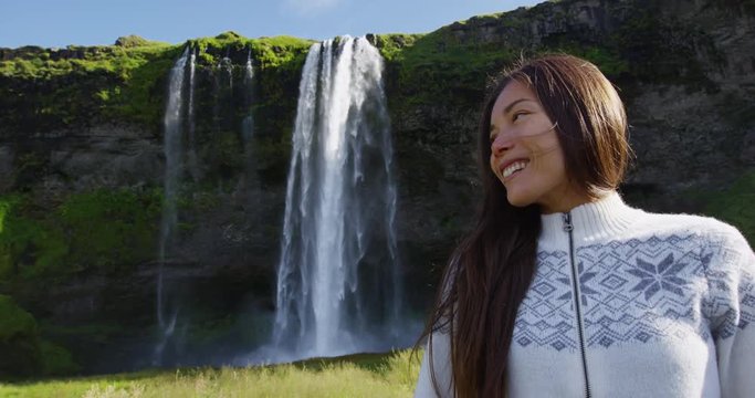 Woman on Iceland in Icelandic sweater by waterfall outdoor fun. Candid beautiful female model in nature landscape with tourist attraction Seljalandsfoss waterfall on Ring Road.