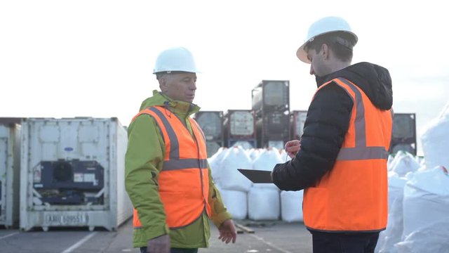 Two engineers wearing hardhats talking together while sign up documents on a large commercial trainyard tracking inventory, shaking hands.