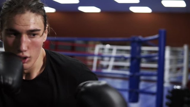 Close up footage of determinated kickboxer hits boxing pear. An angry boxer puts a punch in a boxing bag in black gloves. Workout in the gym. Slow motion