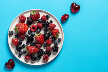Top view plate with variety of forest fruits, berries and hearts on a blue background
