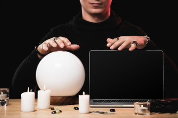 cropped view of oracle near laptop with blank screen isolated on black