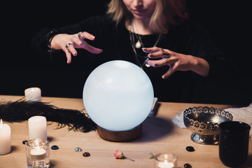 cropped view of female esoteric holding hands above crystal ball isolated on black