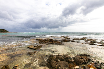 Fototapeta na wymiar Caribbean bay with rocks, sandy beach and coral reef. clear sea of a coral reef beach with beach and clouds on the horizon and waves crashing on the shore