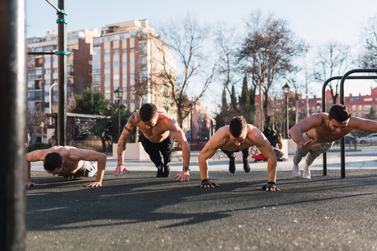 Young athletic men doing push up exercises in park