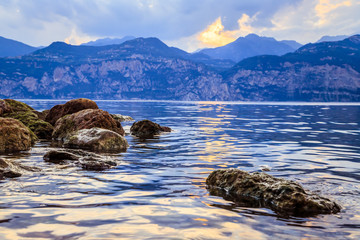 Colorful rocks in the water: Lago di garda at the evening, reflections on the water