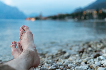 Man is sitting on the beach and enjoying the view over a lake, evening