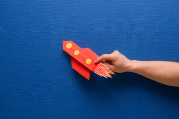 male hands hold a rocket from paper on a blue background