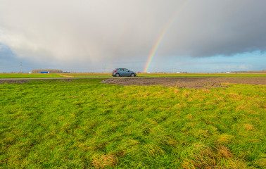 Car parked on a roadside along a meadow below a rainbow in winter