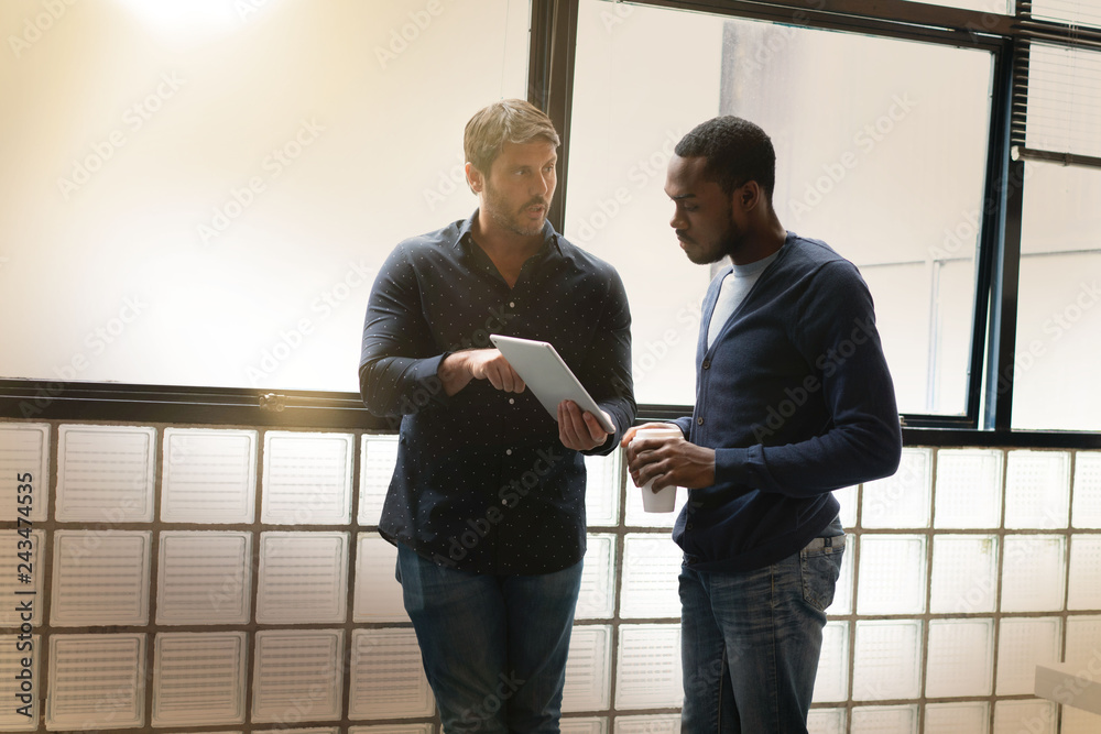 Wall mural colleagues standing together in modern office going over ideas on tablet