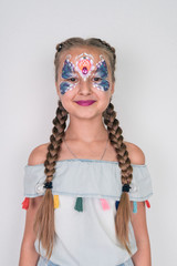 Charming girl with a blue butterfly painted on her face, on white background. face painting