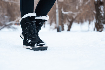 Black winter women's boots with white fur and white soles on the snow in the park