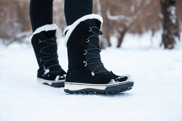 Black winter women's boots with white fur and white soles on the snow in the park
