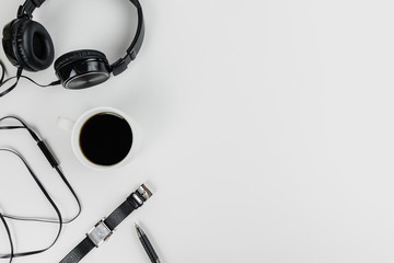 Top view on a freelancer's workspace. White table top with black headphones, watch, pen and cup of coffee. Flat lay with copy space.