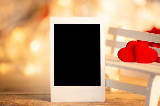 Concept of Valentine, anniversary, wedding greeting with a picture frame, heart shapes on a white wooden bench, bokeh background, close up