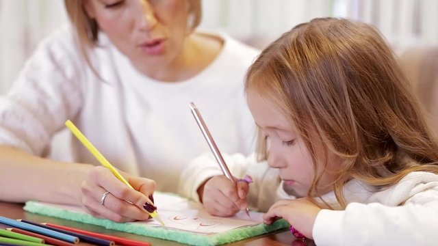 Close-up Side View Of A Little Beautiful Girl Draws With Her Mother Sitting At The Coffee Table. Concept Of Joint Developmental Activities With Children