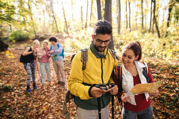 Cute couple looking at compass. Woman holding map while the rest hikers standing in the background...