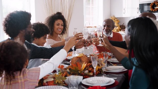 Multi generation mixed race family raising glasses to make a toast sitting at their Thanksgiving dinner table, close up
