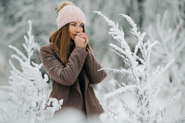 Portrait of blonde woman in hat looking at camera on walk in winter forest