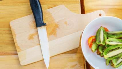 White knife with kiwi and tomato fruits on wooden floor