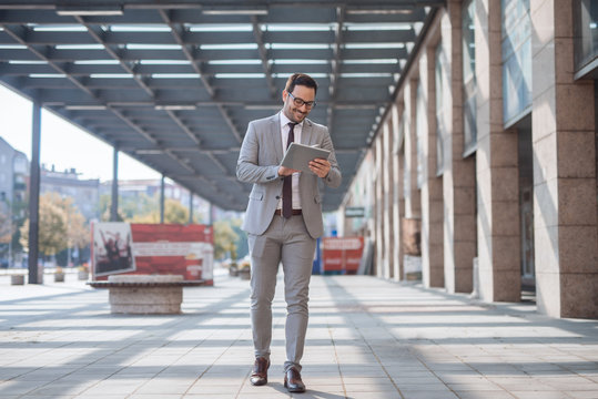 Businessman walking on the street and using tablet to check an e-mail. In background business center exteriour.