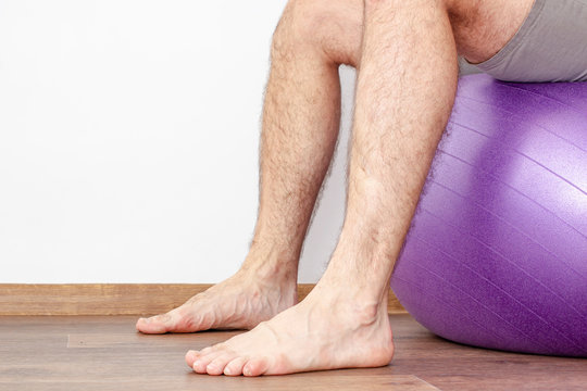 Man with hairy legs sitting on a fitness ball. Close-up.