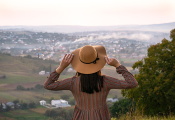 Girl in hat from behind looks at the city at sunset